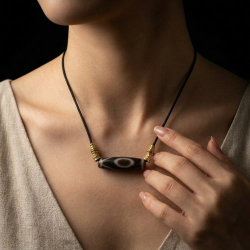 Woman wearing the Calm Witness Dzi Agate grounding necklace, showcasing the substantial 46.5mm cylindrical focal stone resting horizontally against her chest over a neutral linen dress.