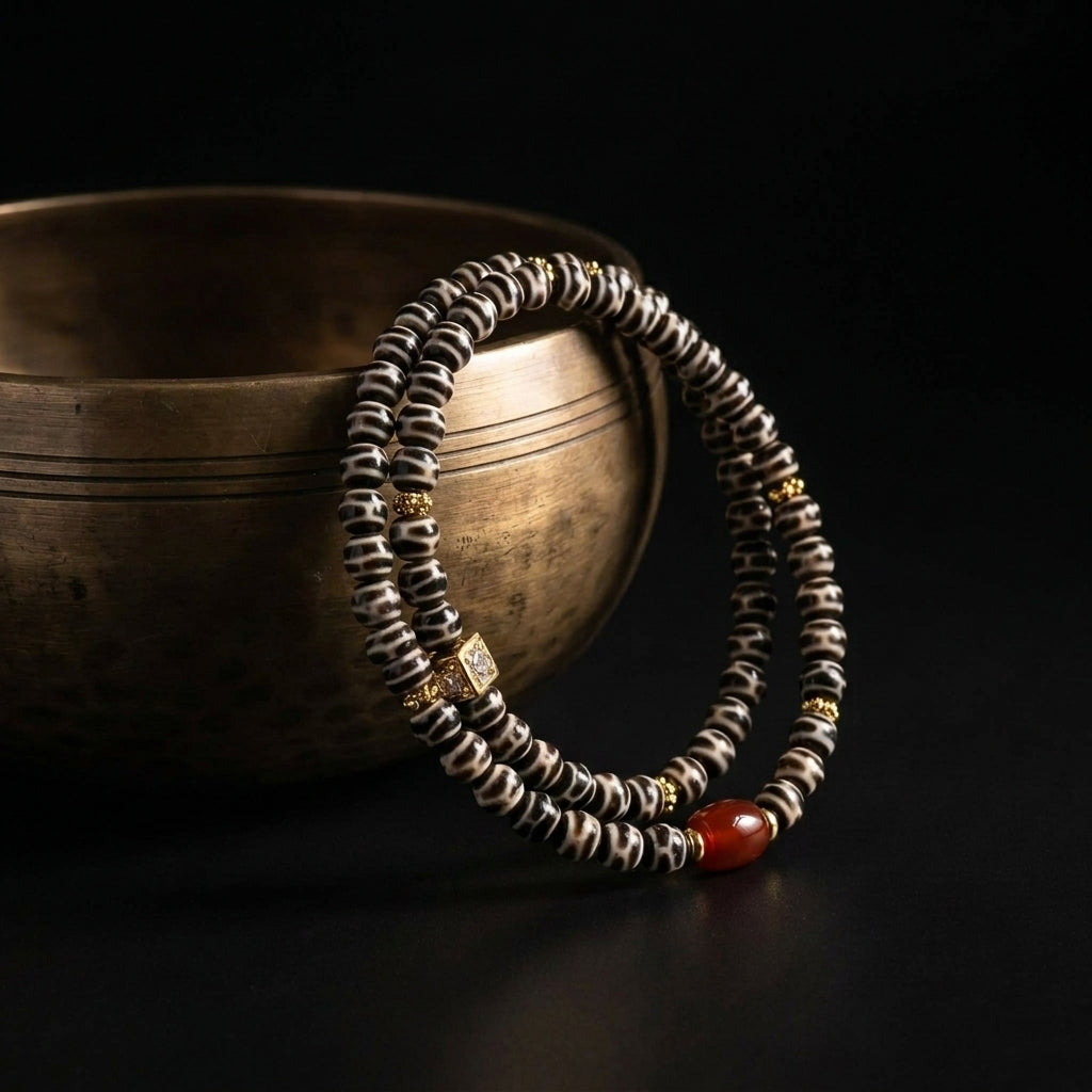 The Defined Path patterned Agate focus bracelet resting beside an antique brass bowl, highlighting the rhythmic black and white banding and geometric gold accents in soft, dramatic lighting.
