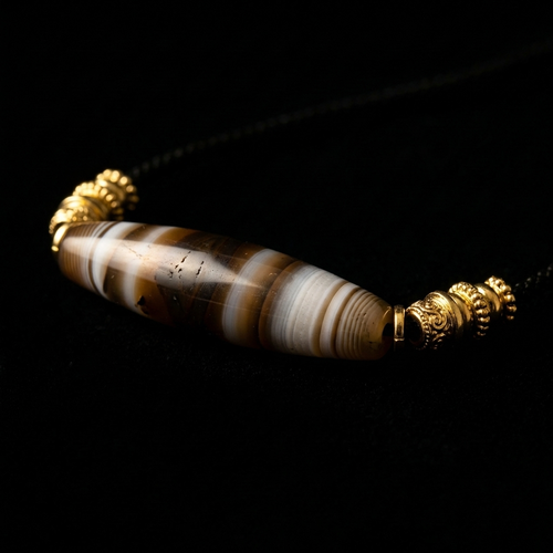 Close-up of the Earth Horizon Banded Agate grounding necklace, featuring a 50mm smooth cylindrical stone with ancient earth-toned strata and 18K gold ribbed spacers.