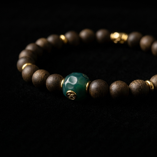 Close-up of the First Leaf Agarwood focus bracelet, featuring 8.4mm resin-dense wooden beads, 18K gold spacers, and a faceted green focal node with a golden emblem.