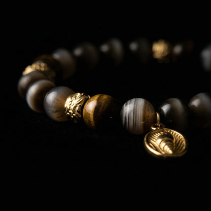 Close-up of the Tiger's Eye focus bracelet on a dark background, featuring smooth, polished natural stones and a matte 18K gold charm.