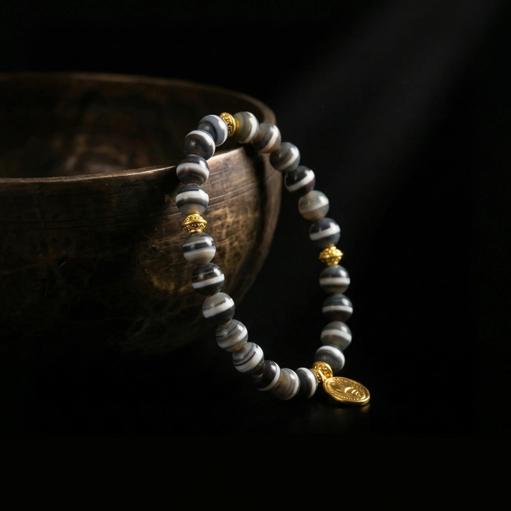The Single-Line Agate balancing bracelet resting near an antique singing bowl, representing Jambhala's 1,900-meter acoustic purification ritual.