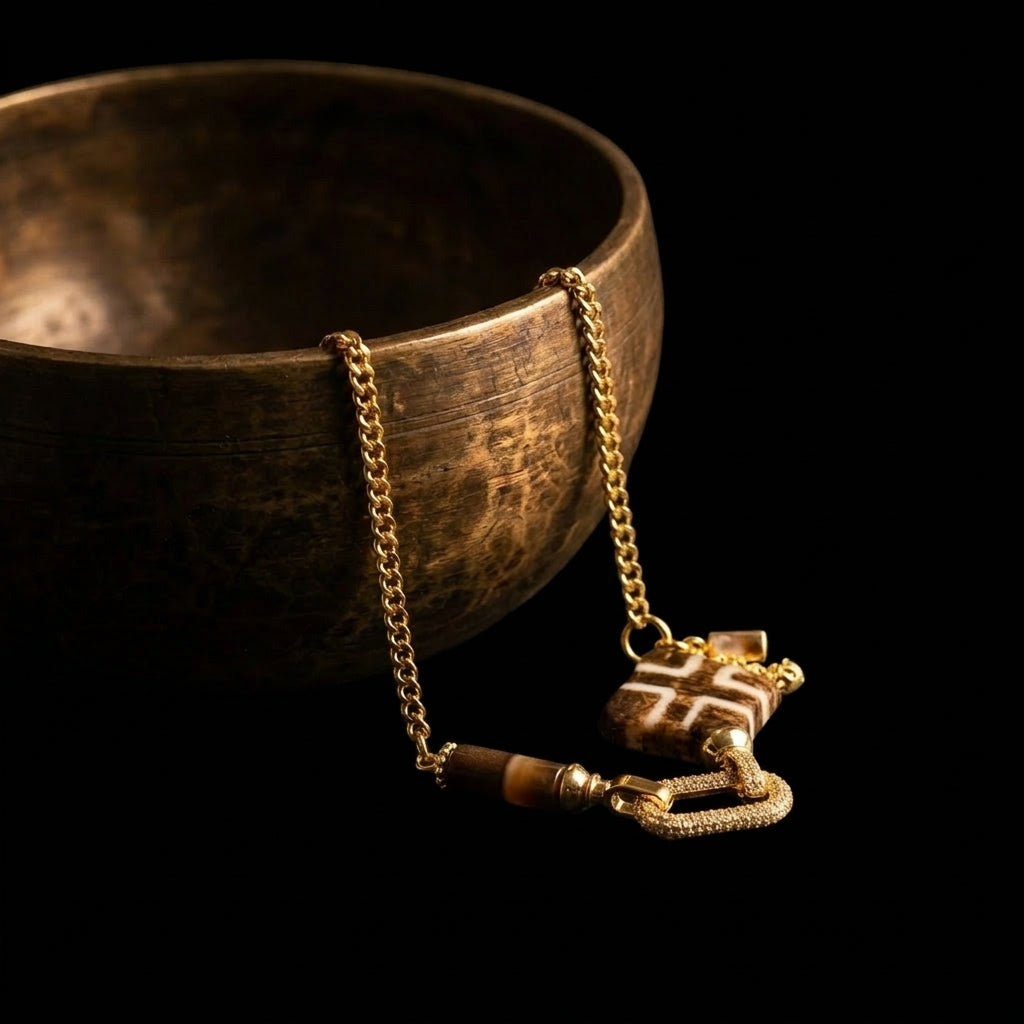 The Steady Link Pumtek and Agate grounding necklace resting beside an antique brass bowl, highlighting the flat-cut fossil and robust gold curb chain in dramatic lighting.