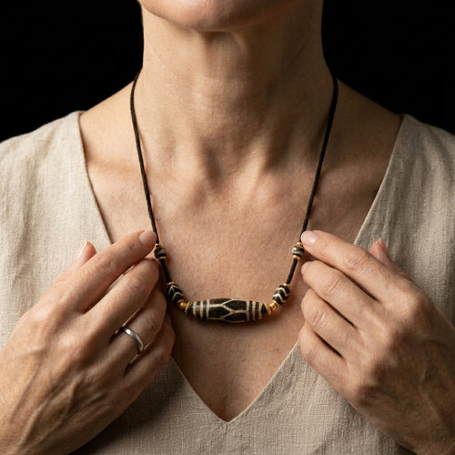 A person adjusting the heavy Petrified Wood necklace on their chest, using the fossilized stone as a physical barrier against sensory overload.