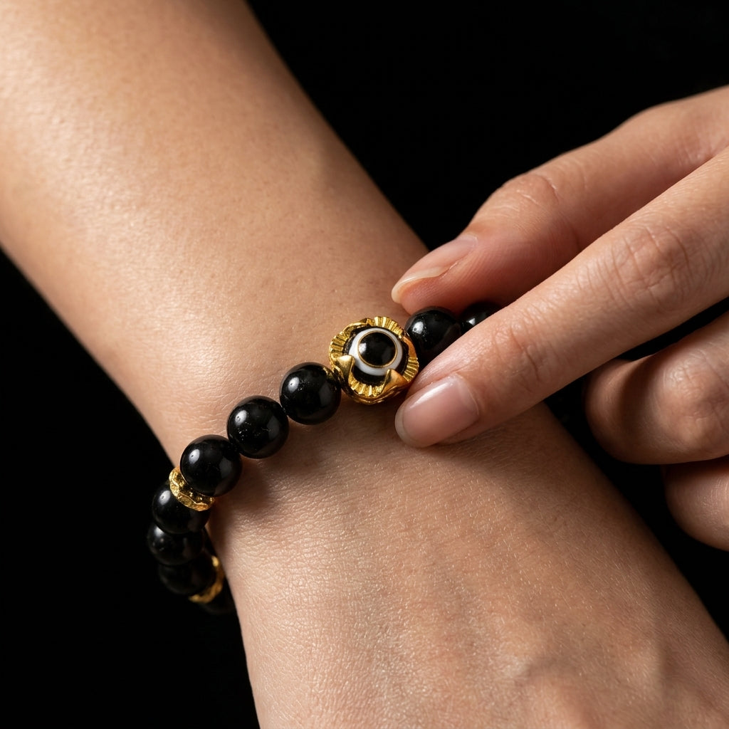 A person pressing their thumb against the gold and black sentinel bead of the Obsidian bracelet, using the hard volcanic glass to maintain a physical