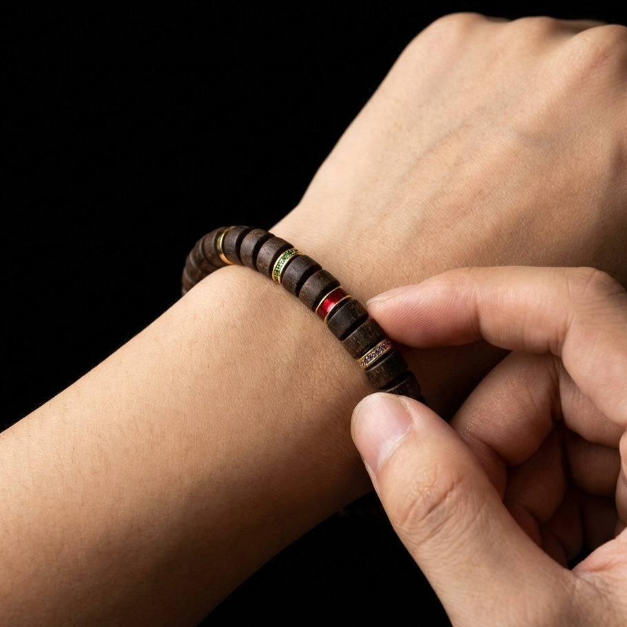 Person touching the red focal node of the Huanghuali wood bracelet on their wrist, using it as a tactile cue to break emotional numbness.