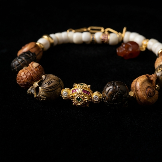 Close-up of the Memento Mori grounding bracelet, featuring multi-material hand-carved skulls, white bone beads, an ornate 18K gold focal sphere with ruby and emerald pavé accents, and a red agate skull charm.