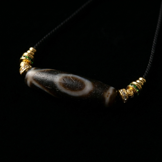 Close-up of the Himalayan Dzi bead grounding necklace, featuring a massive 46.5mm cylindrical agate with the eye motif and 18K gold spacers with green and clear pavé crystals.
