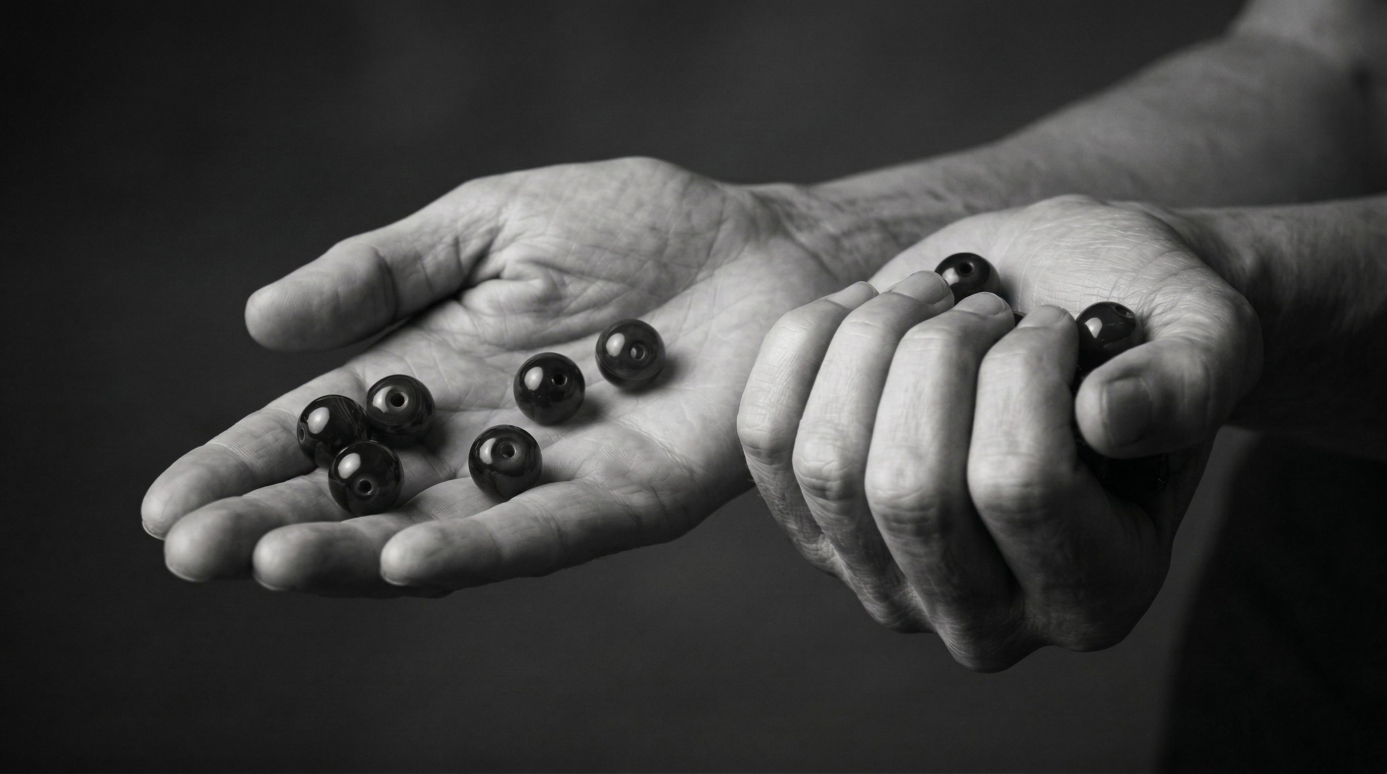 Black and white close-up of hands holding smooth, polished dark grounding stones, capturing the tactile physical act of using a wearable worry stone for everyday somatic anxiety relief.