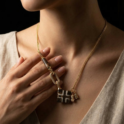 A person touching the pavé interlocking link on their geometric Pumtek grounding necklace, using the heavy architectural centerpiece as a physical switch to overcome scarcity.