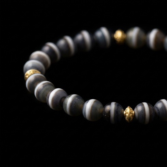 Close-up of the Single-Line Agate balancing bracelet, featuring 8.3mm dark stones with natural white equatorial stripes, 18K gold spacers, and a golden charm.