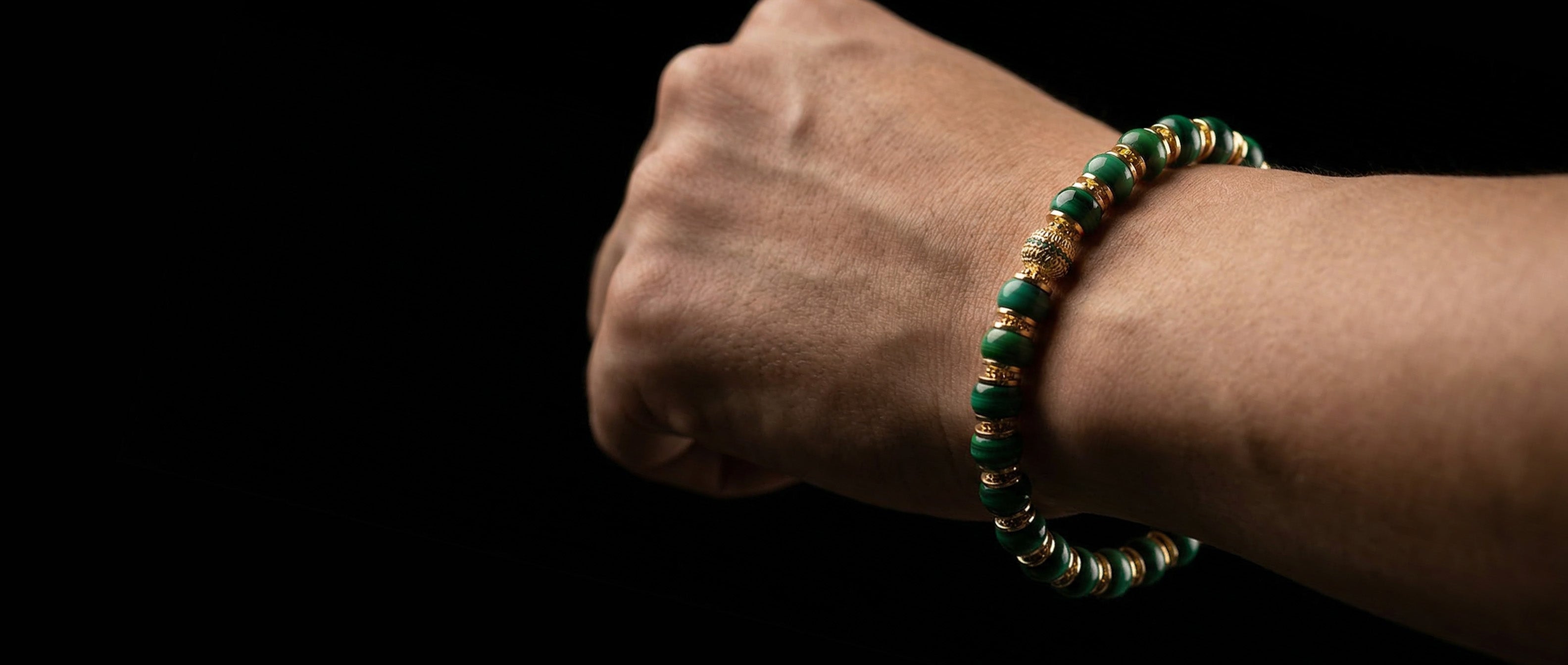 A person wearing the deep green Malachite renewal bracelet on their wrist, showcasing precision disc-cut stones with concentric banding and an ornate 18K gold focal node, used as a tactile switch for cognitive inertia.2