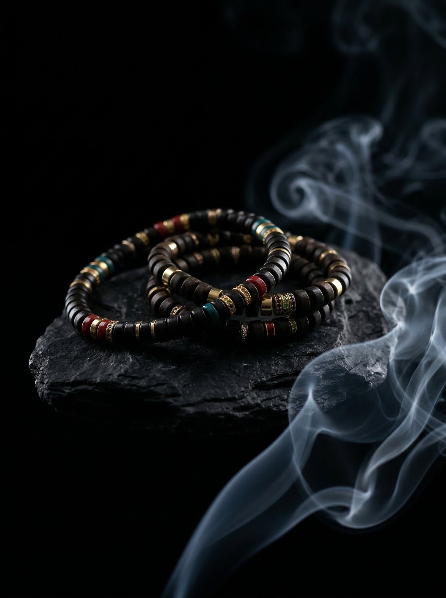 Multi-wrap dark wood grounding bracelet resting on a rugged black stone amidst thick, swirling smoke. This dark wabi-sabi aesthetic highlights the earthy wooden beads as a heavy tactile and olfactory anchor, designed to cut through daily mental fog.