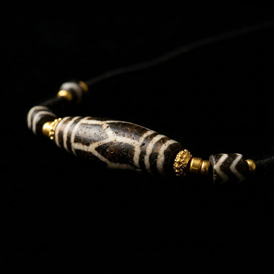 Close-up of the Petrified Wood Pumtek grounding necklace, featuring a dark fossilized cylindrical bead with white geometric motifs, 18K gold spacers, and banded agate nodes.