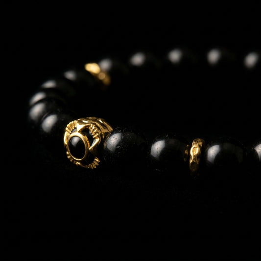 Close-up of the Black Obsidian protection bracelet, featuring high-gloss volcanic glass beads and an 18K gold-plated sentinel focal node on a dark background.