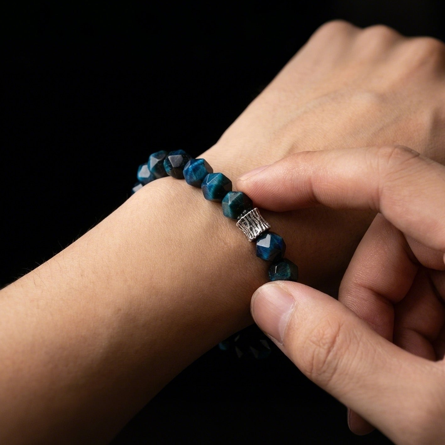 A person touching the oxidized silver-toned metal accent on their faceted Turquoise grounding bracelet, used as a physical override for reactive anxiety.